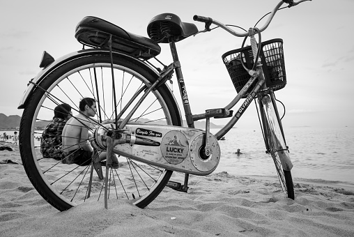 Nha Trang, Vietnam - July 7, 2007: A Japanese-made bicycle is parked on the beach in Nha Trang, Vietnam. Two Vietnamese friends sit together in the background.