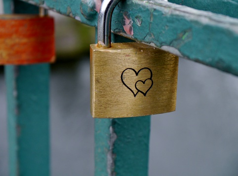 A metal lock with heart engraving hangs on a bridge railing