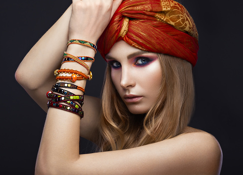 Beautiful fashion girl in a scarf and bracelets boho style. Beauty face, bright trendy makeup. Picture taken in the studio.
