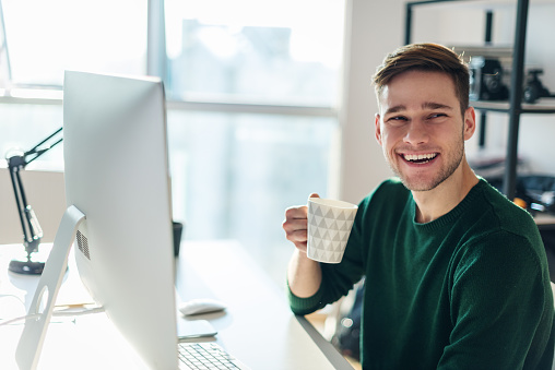 Shot of an attractive young businessman drinking a coffee while working on a computer.
