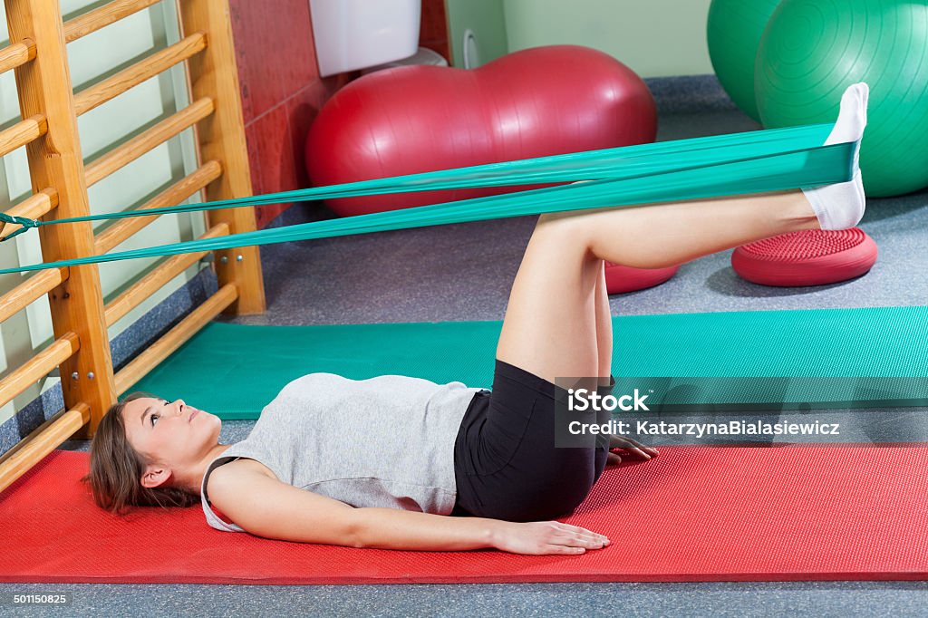 Girl lying on exercise mat and stretching legs Girl lying on exercise mat and stretching legs with elastic band Exercising Stock Photo