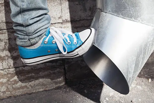 Teenager in blue sneakers kicks drainpipe, aggression concept