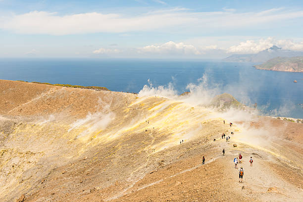 steaming volcanic crater, vulcano, Sicily, Italy steaming volcanic crater, vulcano, Sicily, Italy. unrecognizable people walking on the edge of the crater. Mt. Etna in far distance. mt etna stock pictures, royalty-free photos & images