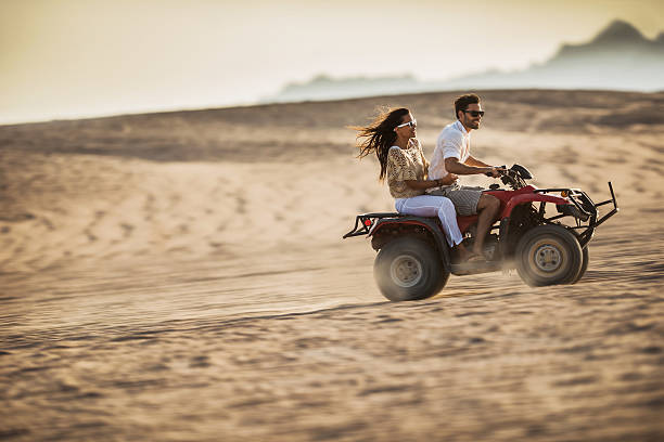 feliz pareja joven divirtiéndose mientras por pasear en bicicleta. - off road vehicle quadbike desert dirt road fotografías e imágenes de stock