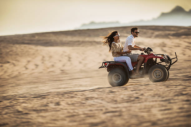jovem casal feliz divertir-se durante a condução em quad bike. - off road vehicle quadbike desert dirt road imagens e fotografias de stock