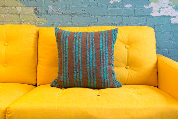 Close up of yellow fabric sofa and cushions with vintage style against blue bricks wall.