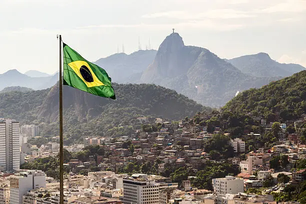 Brazilian flag in front of Corcovado mountain and low/high wealth buildings.