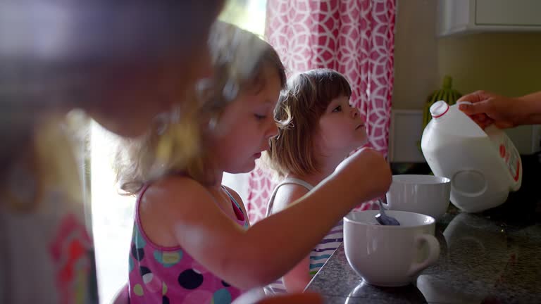 A mother pours milk into her daughters' cereal bowls