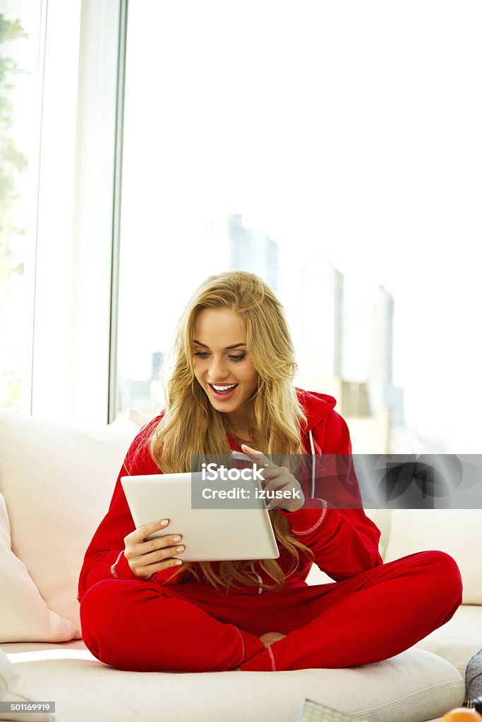 Young woman with digital tablet Young woman sitting on sofa at home and using a digital tablet in the morning. 20-24 Years Stock Photo