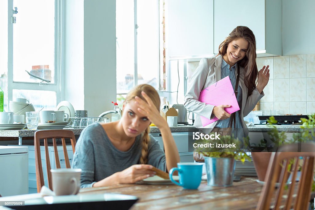 Students lifestyle Worried young woman eating breakfast in the kitchen while her friend going out. Envy Stock Photo