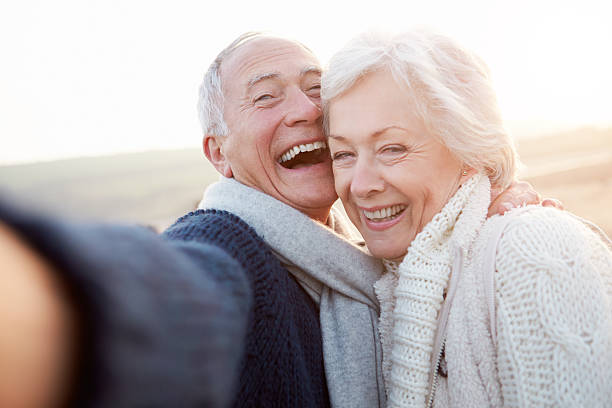 sênior casal em pé na praia tirando selfie - retirement couple beach senior adult - fotografias e filmes do acervo