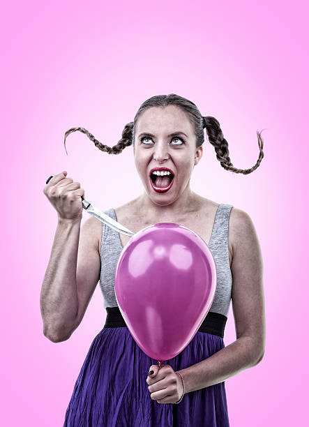 Angry Young Woman Bursting a Balloon with a Knife stock photo