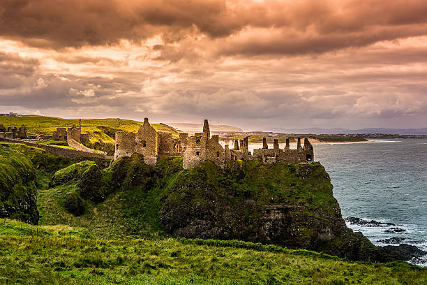 Dunluce Castle Dunluce Castle is a now-ruined medieval castle in Northern Ireland. It is located on the edge of a basalt outcropping in County Antrim (between Portballintrae and Portrush), and is accessible via a bridge connecting it to the mainland. The castle is surrounded by extremely steep drops on either side, which may have been an important factor to the early Christians and Vikings who were drawn to this place where an early Irish fort once stood. belfast photos stock pictures, royalty-free photos & images
