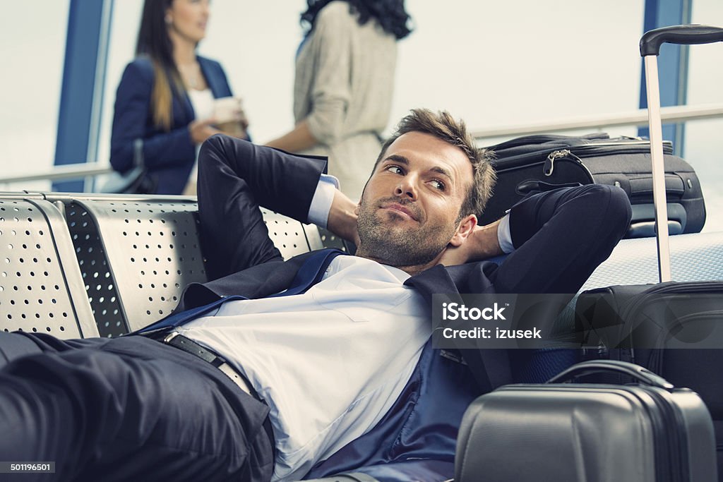 Waiting for the flight People waiting for a flight at the airport lounge. On the foreground businessman lying down on bench next to the heap of suitcases. Men Stock Photo