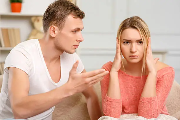 Bad time. Young frowning woman covering her ears while boyfriend is explaining something to her. 