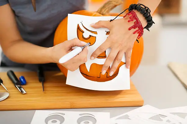 Photo of Woman using stencils to carve pumpkin Jack-O-Lantern. Closeup