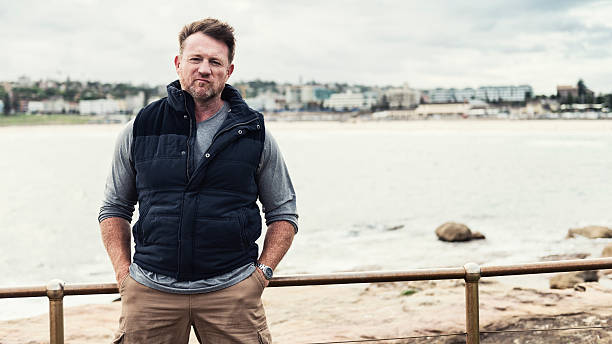 Tough guy Color portrait of a mature, rugged, tough Australian man with Bondi Beach of Sydney in the background. 16x9 letterbox format with copy space on right. machos stock pictures, royalty-free photos & images