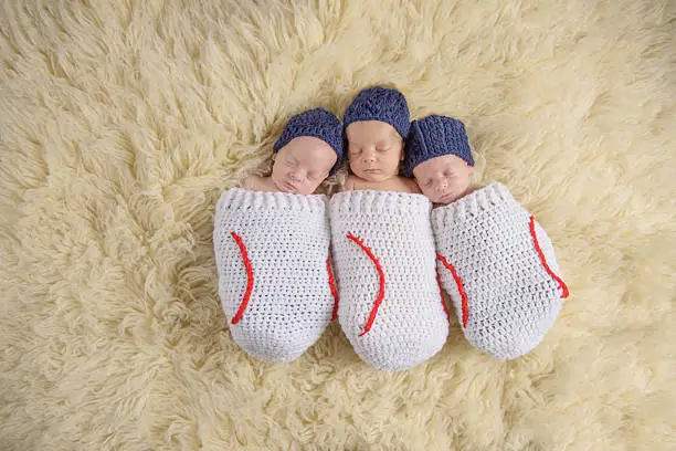 Newborn triplets swaddled in baseball themed cocoon.