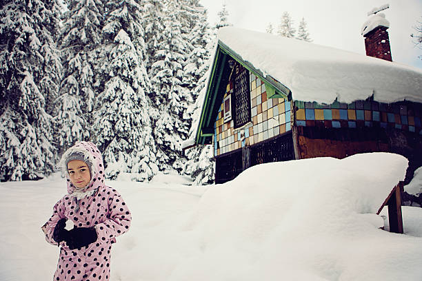 Little girl is holding snowball at the front of the chalet in the snowy mountain.