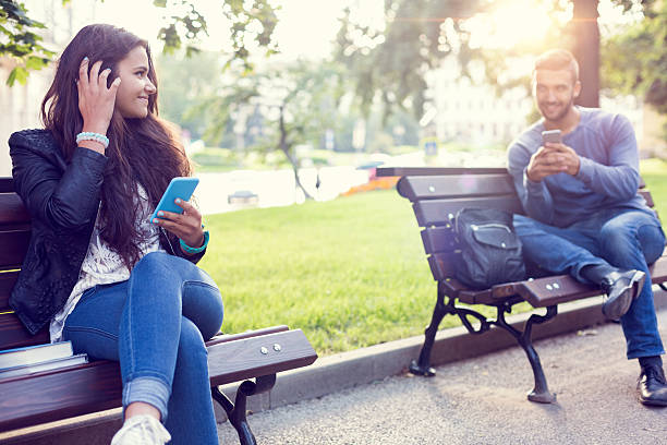 Flirting couple in the park Happy couple using smartphones in the city park flirting stock pictures, royalty-free photos & images