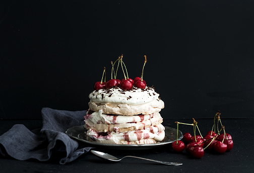 Pavlova cake with fresh cherry, cheese cream and chocolate chips in vintage silver plate over dark grunge backdrop