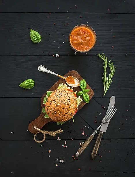 Photo of Fresh homemade burger on dark serving board with spicy tomato