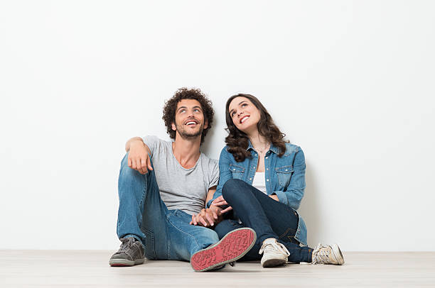 Happy Young Couple Looking Up Portrait Of Happy Young Couple Sitting On Floor Looking Up Ready for your text or product two people thinking stock pictures, royalty-free photos & images