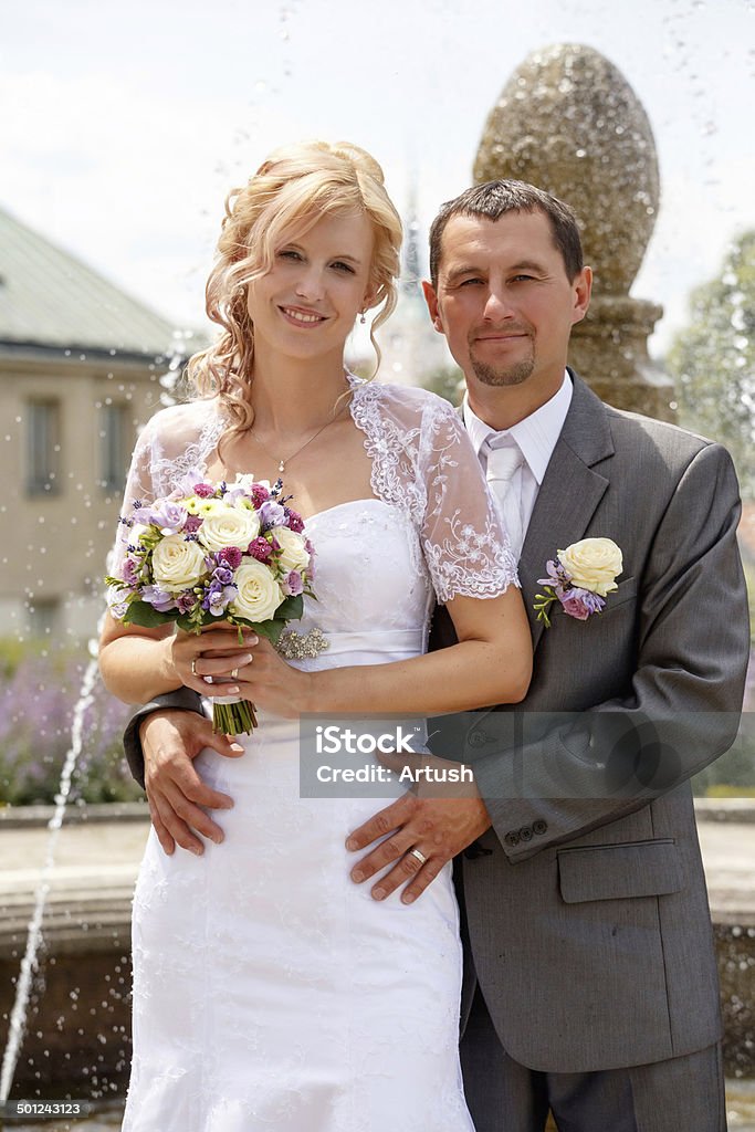 beautiful young wedding couple beautiful young wedding couple, blonde bride with flower and her groom against fountain Adult Stock Photo