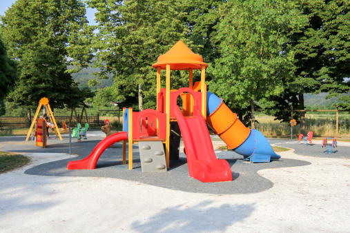 Children riders on wooden swing with spring on the playground in the park. Two girls ride on the playground in summer