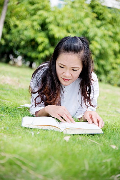 Asian woman lying on green grass and reading a book.