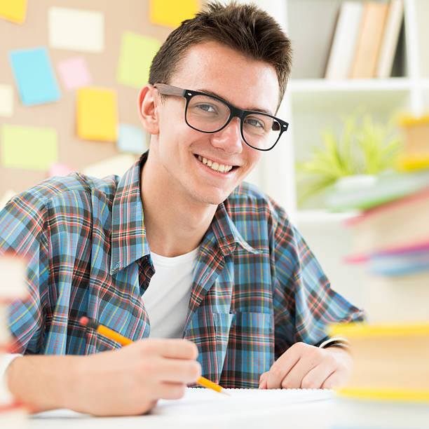 Smart teenage student Happy teenage student surrounded with books posing to camera nerd teenager stock pictures, royalty-free photos & images