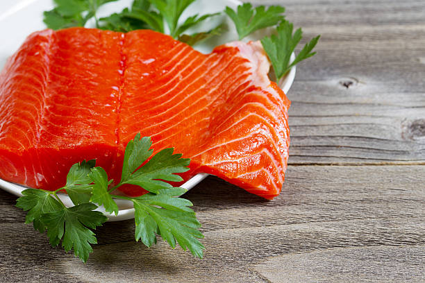 Fresh Fillet of Sockeye Salmon with parsley Closeup horizontal photo of fresh sockeye salmon fillet, partially out of plate, with parsley on the side and rustic wood underneath sockeye salmon filet stock pictures, royalty-free photos & images