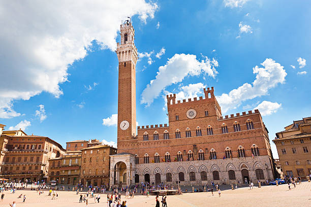 Torre del Mangia, Palazzo Pubblico, Piazza del Campo, Siena, Italy The Piazza del Campo, the public town square of the city of Siena, Tuscany, Italy, features the Palazzo Pubblico museum and its bell tower, the Torre del Mangia. The clam shell shaped piazza is a tourist destination, with street venders, restaurants, hotels, and retail shops. Horizontal cityscape with copy space. torre del mangia stock pictures, royalty-free photos & images