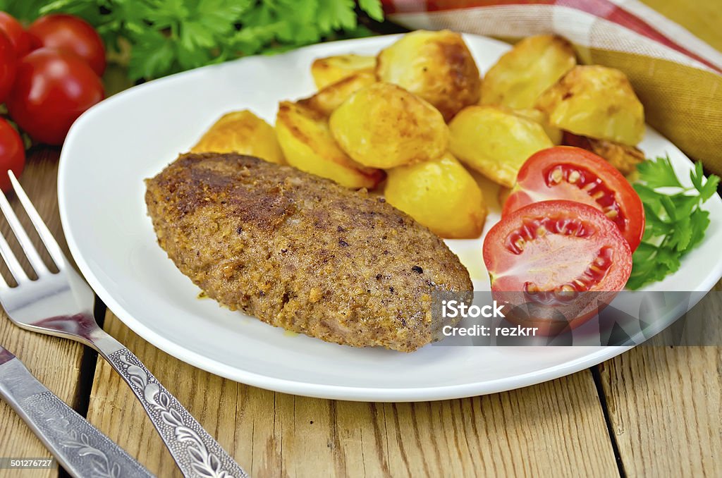 Cutlet meaty with fried potato Cutlet meat with roasted potatoes, tomatoes and dill on a plate, parsley, napkin on wooden board Breaded Stock Photo