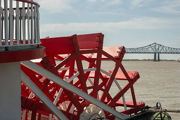 Looking at red paddlewheel and back at the Crescent City Connection bridge in New Orleans.  This is the farthest downstream bridge on the Mississippi River.  There’s copy space in upper part of frame.  New Orleans is a top US tourist destination and famous for its music, food, lifestyle and history.