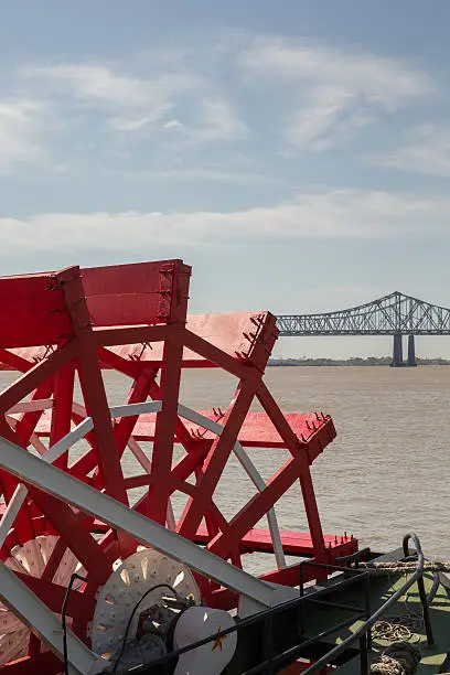 Looking at red paddlewheel and back at the Crescent City Connection bridge in New Orleans.  This is the farthest downstream bridge on the Mississippi River.  There’s copy space in upper part of frame.  New Orleans is a top US tourist destination and famous for its music, food, lifestyle and history.