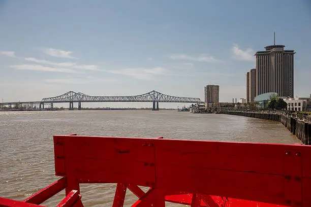 Looking at red paddlewheel and back at the Crescent City Connection bridge in New Orleans.  This is the farthest downstream bridge on the Mississippi River.  There’s copy space in upper part of frame.  New Orleans is a top US tourist destination and famous for its music, food, lifestyle and history.