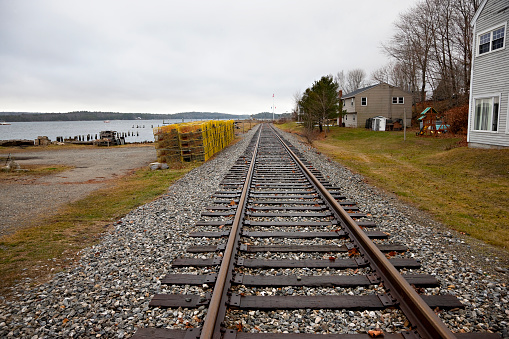 Wiscasset, Maine, USA -- December 10, 2015: Railroad tracks along Wiscasset waterfront, Maine. Residential district is on the right, fishermen equipment, boats, lobster traps are on the left. Typical coastal New England scenery.