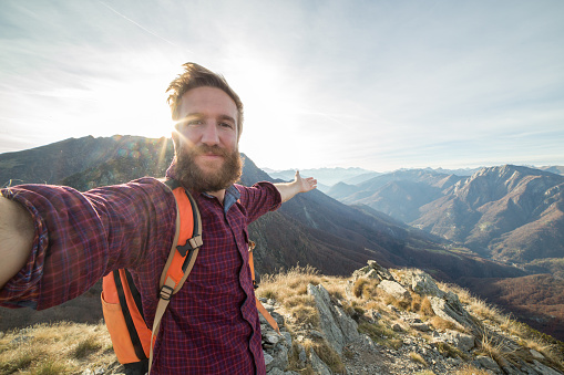 Young man hiking reaches mountain top and takes selfie portrait