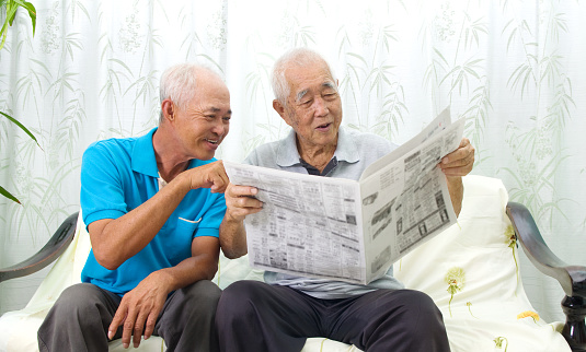 Portrait of chinese family reading newspaper together at home. Mature 70s senior man and his son