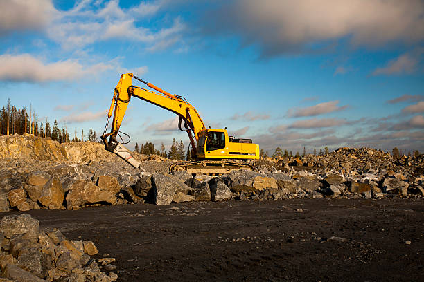 Yellow excavator with hydraulic hammer is working in gravel pit in sunny day.
