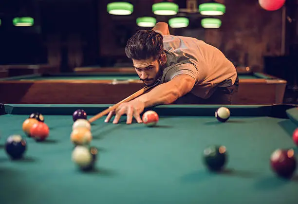 Photo of Concentrated man aiming at pool ball while playing snooker.