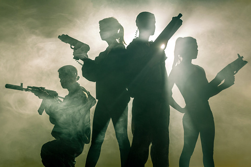 Silhouettes in smoke. Four young people dressed in military clothes. The two women and two men are posing with laser handguns in hands. Studio shooting on green background