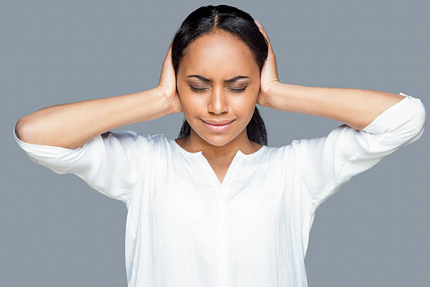 Feeling tired and stressed. Frustrated young African woman covering ears with hands and keeping eyes closed while standing against grey background hands covering ears stock pictures, royalty-free photos & images