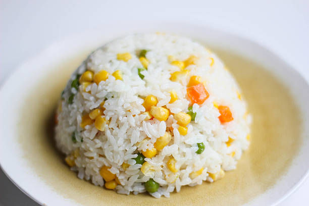 Risotto (Pilav or Rice) with Vegetables Homemade risotto, cooked with carrot, beans and corn, shaped by a bowl, served on a sandy textured light yellow plate on white background. masala stock pictures, royalty-free photos & images