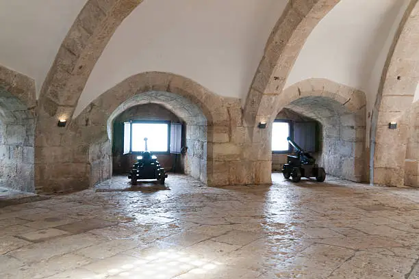 Two canons pointing to the Tagus river in the casemate of Belém Tower. Each canon has its niche. Light enters from portholes and, mainly, from a window in the ceiling.