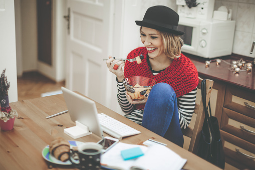 Young woman is having breakfast in the kitchen while she is checking the news on the internet