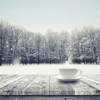 Hot drink in the cup on wooden table over winter snow covered forest. Beauty nature backgroundCup with hot drink on wood table over winter forest  background
