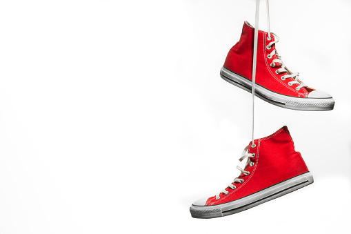 Red pair of canvas sneakers hanging in front of a white background