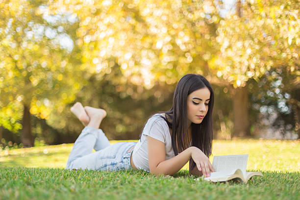 istock Young woman lying down outdoors in the garden reading book 501390098
